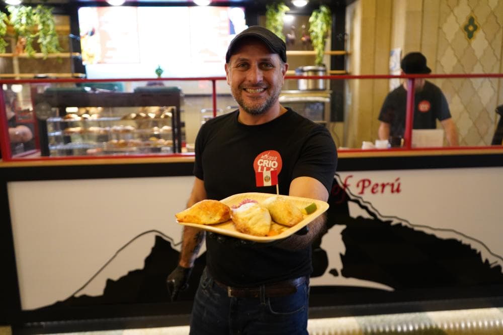 Man is standing holding plate of empanadas in front of restaurant Mikasa Criolla Man is standing holding plate of empanadas in front of restaurant Mikasa Criolla