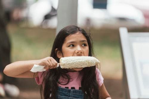 Young girl eating Mexican street corn at Hola Asheville Festival Young girl eating Mexican street corn at Hola Asheville Festival