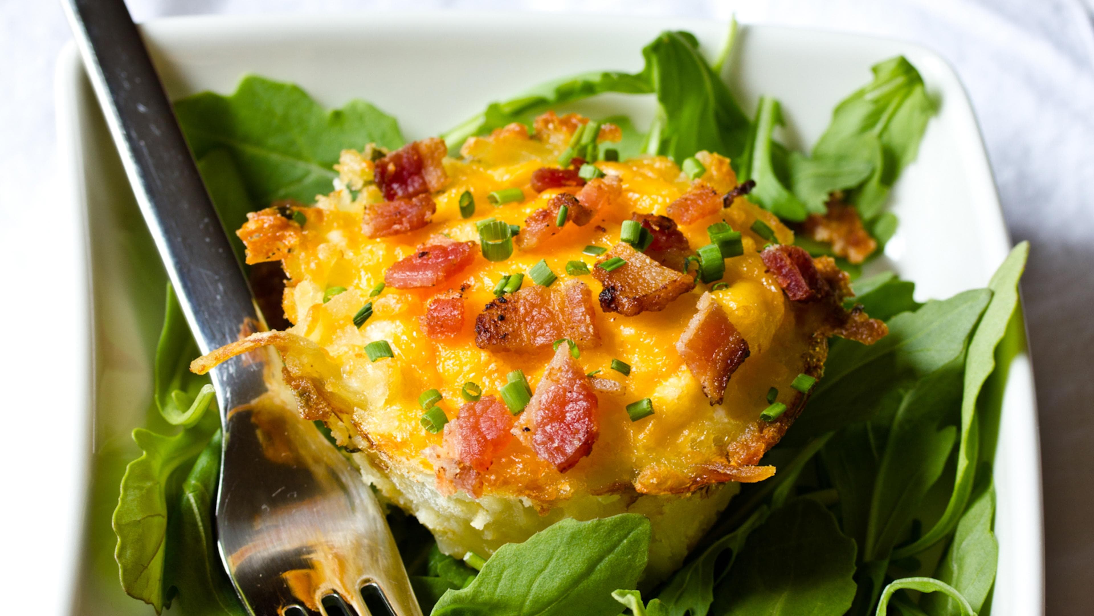 A small egg cup with bacon and chives on top on a bed of greens A small egg cup with bacon and chives on top on a bed of greens