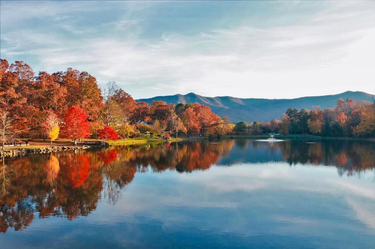 Panoramic view of a lake surrounded by trees with fall foliage colors in the foreground, wispy clouds and a mountain range in the background. Panoramic view of a lake surrounded by trees with fall foliage colors in the foreground, wispy clouds and a mountain range in the background.