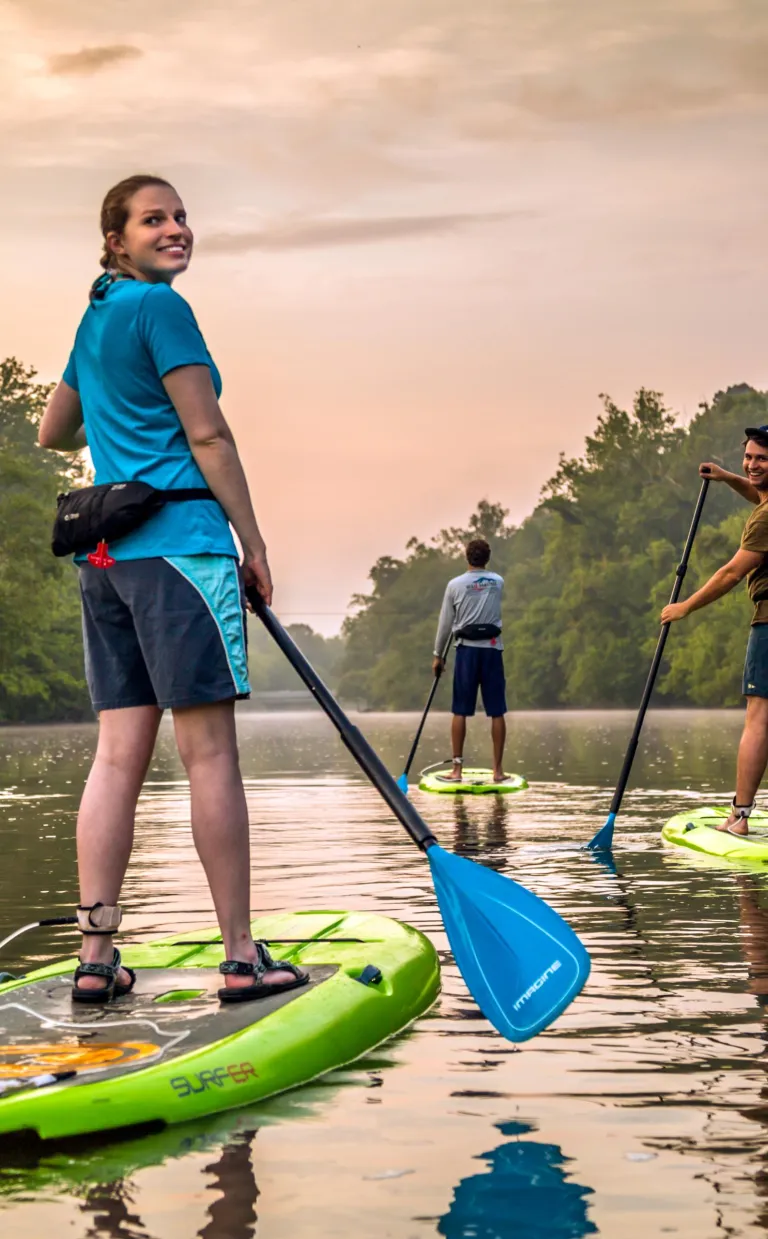 Adventures on the Third Oldest River in the World Three people paddle down an Asheville waterway at sunset