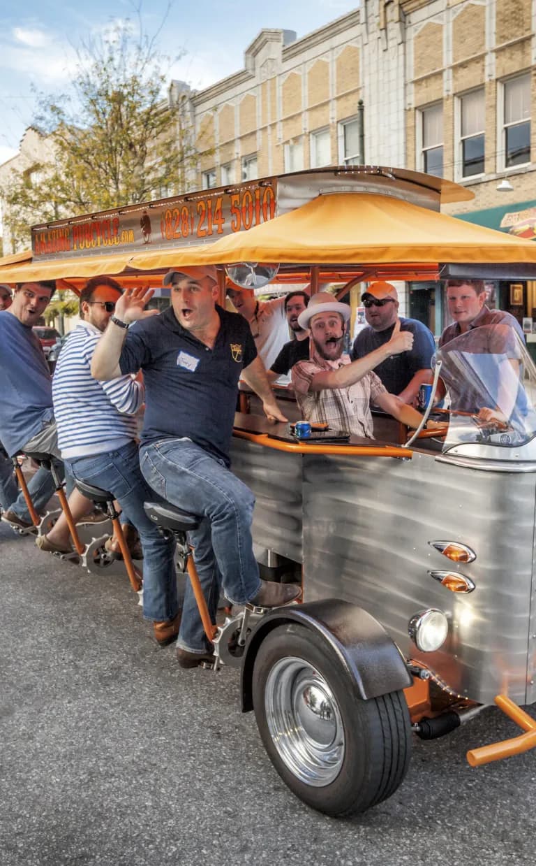 Asheville Beer Tours, Tastings & Tips A group of people laugh as they pedal on a moving bar on a beer tour in Asheville
