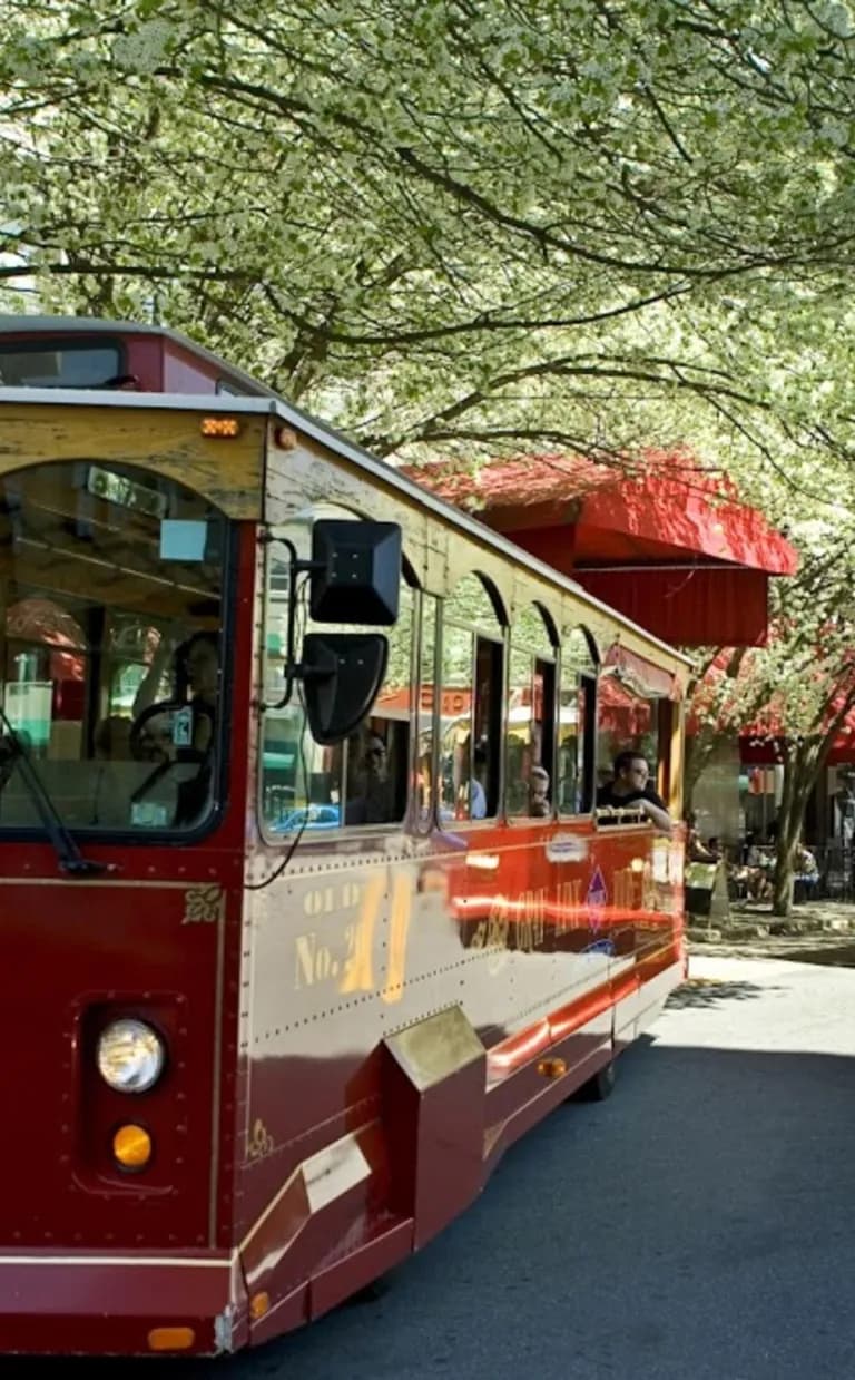 5 Awesome Ways to Explore Asheville’s Rich History a trolly bus is parked on a charming street with green trees in Asheville