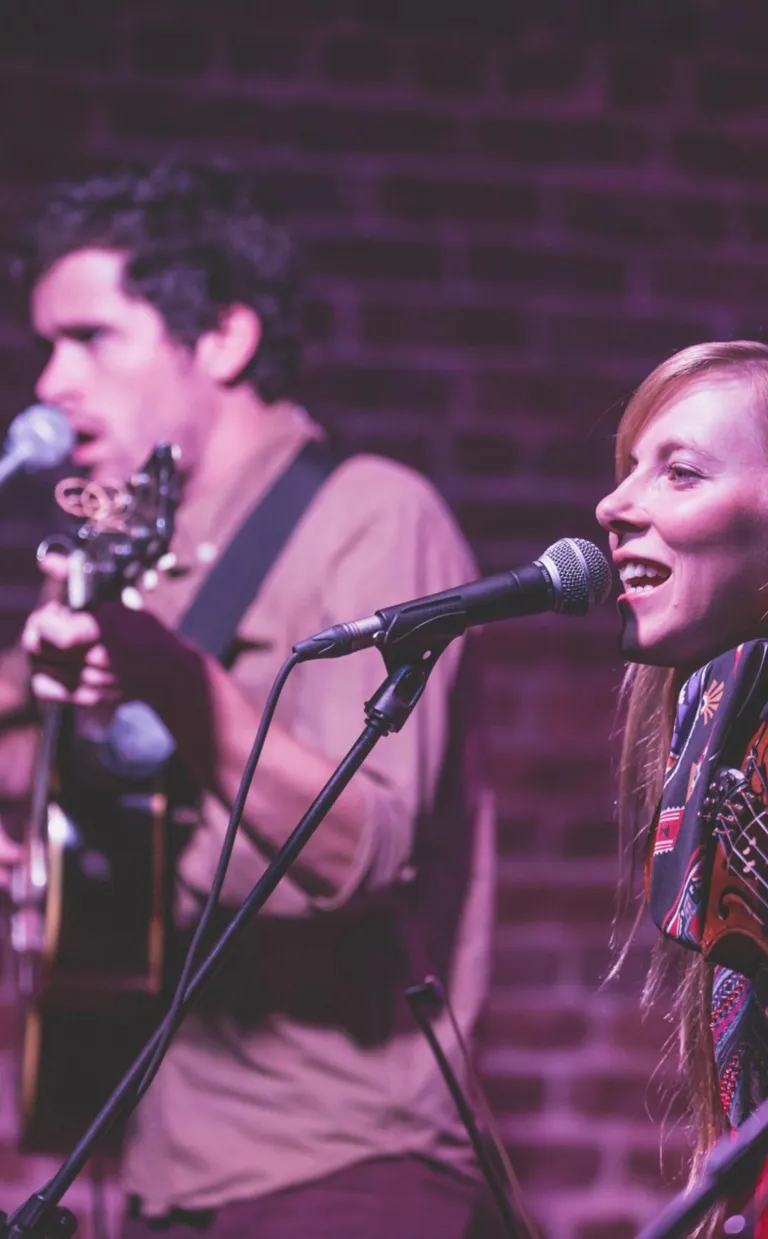 Pickin’ and A-Grinnin’: Where to Find Bluegrass Jams in Asheville, NC two people sing on a stage at a bluegrass concert in Asheville